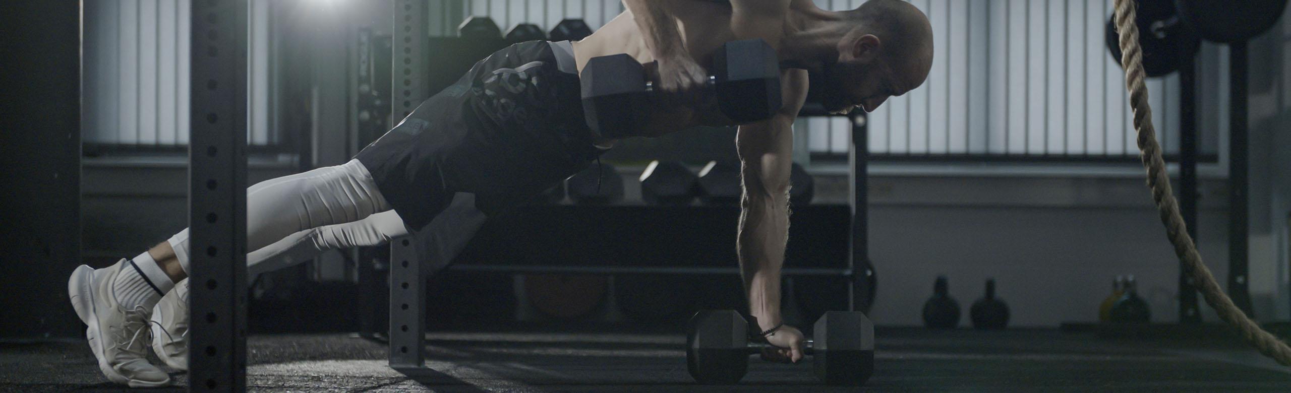 REGUPOL sonusfit - Weight Training A man weight training in a fitness center on REGUPOL sonusfit that combines the field of acoustics with the highest quality athletic flooring.